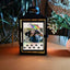 Fotolaterne von Regenbogenspuren, die mit einer Kerze Bilder von einem Hund mit seinem Herrchen anleuchten. Grablaterne steht auf einem Holztisch.
