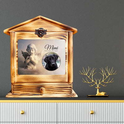 Urne für Hunde aus Holz als Hausmotiv auf einem Regal. Das Bild auf der Hundeurne zeigt ein Labrador und daneben ein Engel.