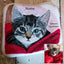 Ein Katzenportrait mit dem Namen auf einem Marmorstein, das eine Hauskatze zeigt, die sich in eine rote Decke einkuschelt. Das Originalbild der Katze steht neben dem Gedenkstein